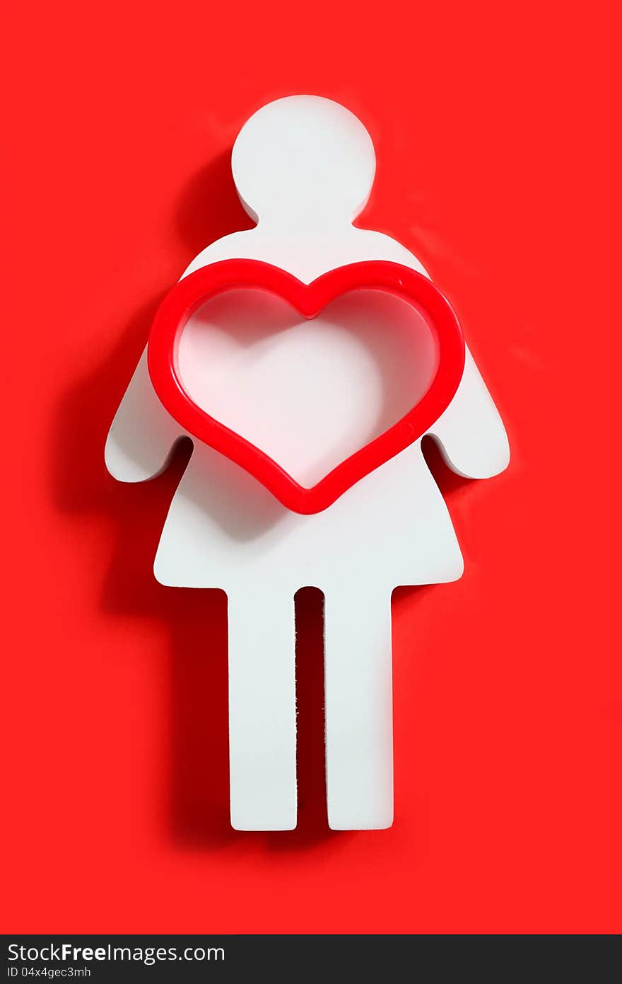 Wooden female figure on a red background with a big red heart on her. Wooden female figure on a red background with a big red heart on her