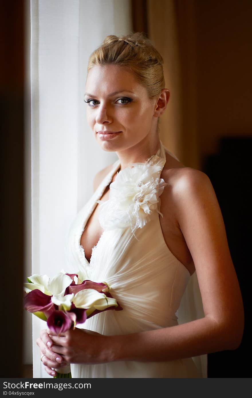 Happy bride with bouquet of calla near sunny window