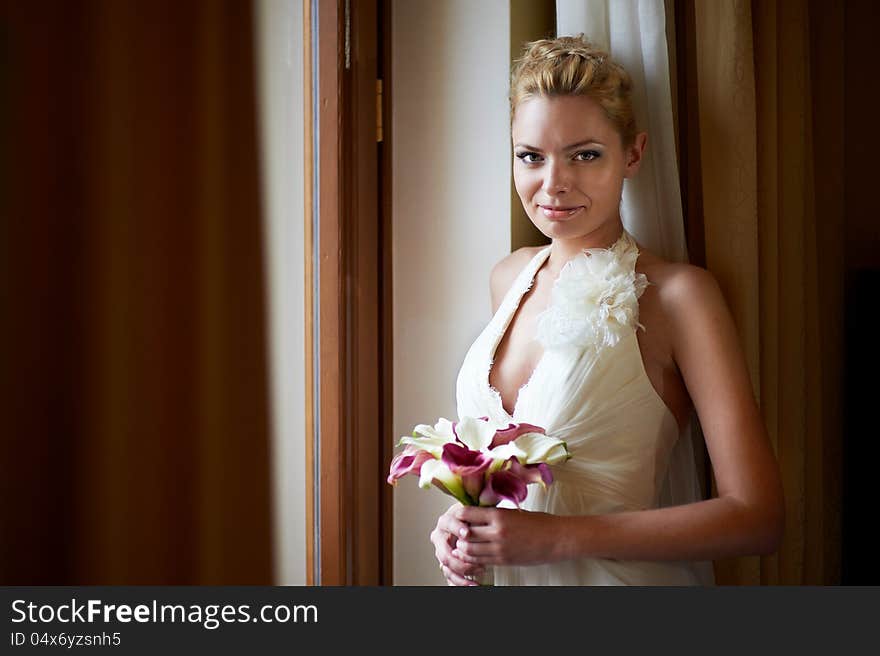 Happy bride with bouquet of calla near sunny window