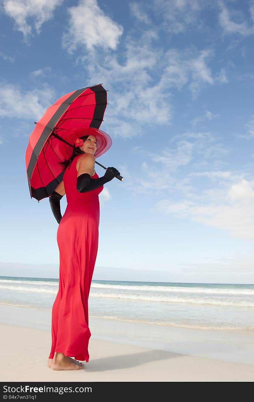 Beautiful looking lady posing happy smiling in elegant red dress, black gloves and umbrella at beach,  with ocean and blue sky as background and copy space. Beautiful looking lady posing happy smiling in elegant red dress, black gloves and umbrella at beach,  with ocean and blue sky as background and copy space.