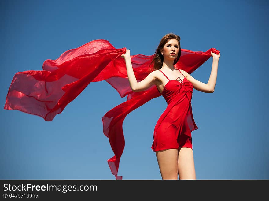 The girl in a red dress with fluttering silk against the blue sky. The girl in a red dress with fluttering silk against the blue sky