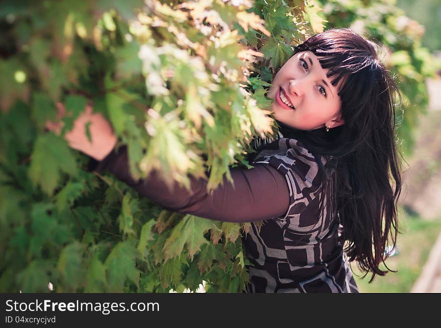 Young woman standing near a maple with lush foliage