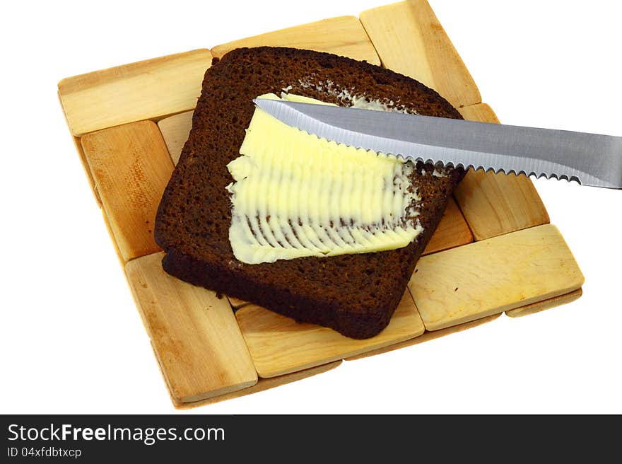 Knife smears butter on a piece of black bread lying on a wooden plank on white. Knife smears butter on a piece of black bread lying on a wooden plank on white