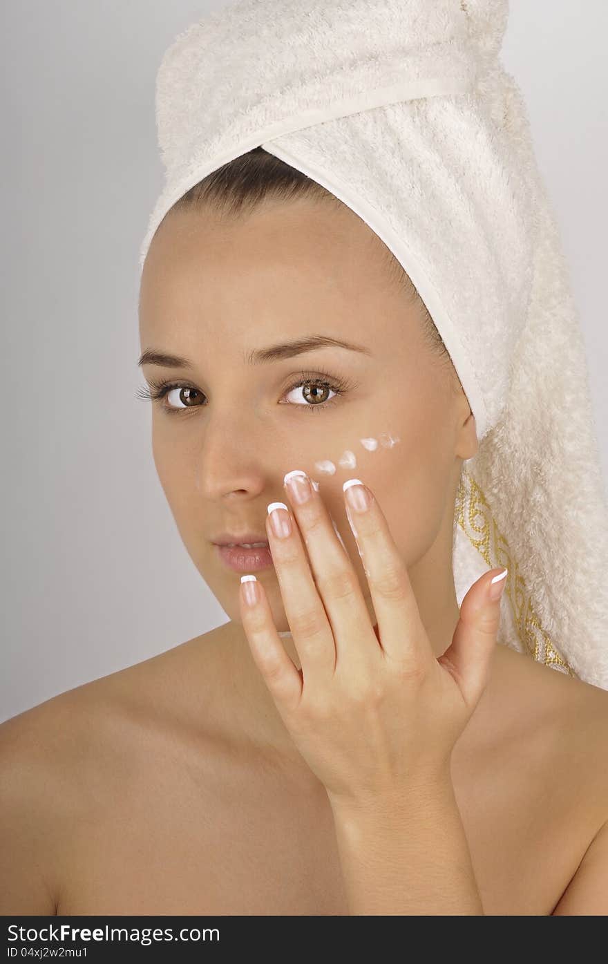 Beautiful woman in a white towel applying moisturizer cream on face. Beautiful woman in a white towel applying moisturizer cream on face.