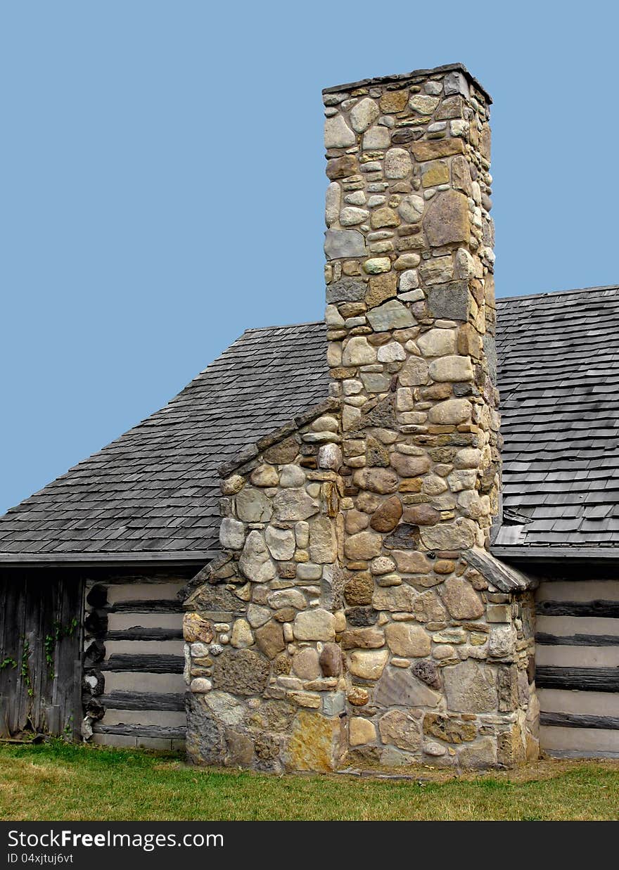 Large chimney made of field stones on the outside wall of a log cabin, against a blue sky. Large chimney made of field stones on the outside wall of a log cabin, against a blue sky.