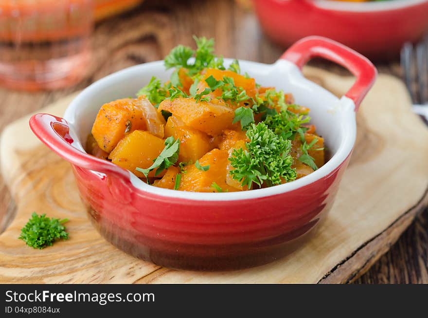 Pumpkin baked in a tomato sauce with garlic and herbs on a wooden board. Pumpkin baked in a tomato sauce with garlic and herbs on a wooden board