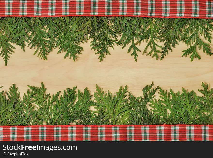 Conifer branches on the wooden light background with plaid red ribbon. Conifer branches on the wooden light background with plaid red ribbon