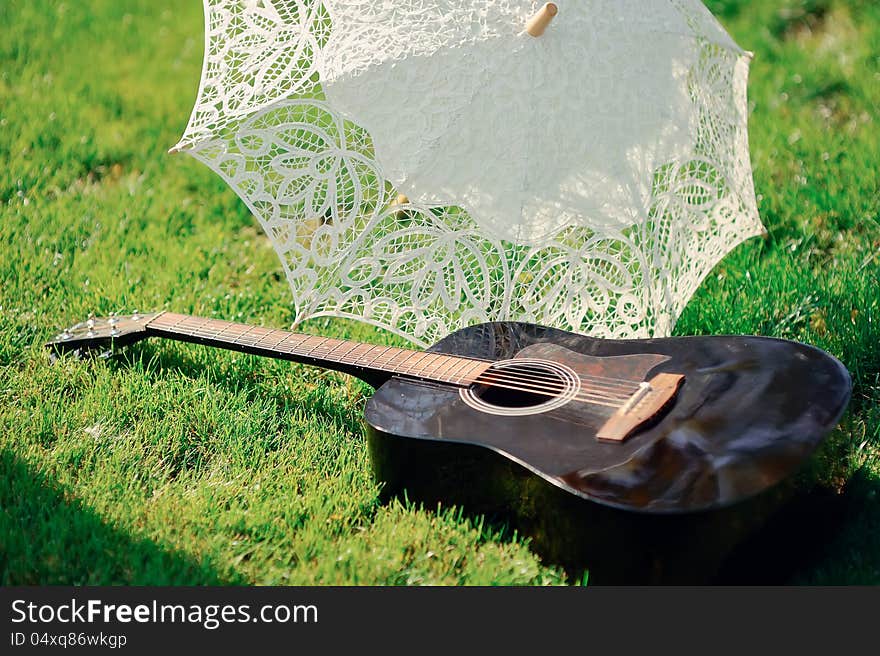 White lacy umbrella and a guitar lying on green grass. White lacy umbrella and a guitar lying on green grass