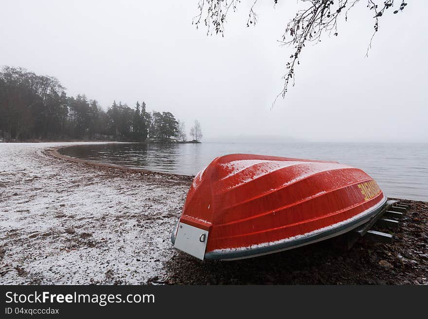 Red rowboat upside down at a snowy beach on a grey day