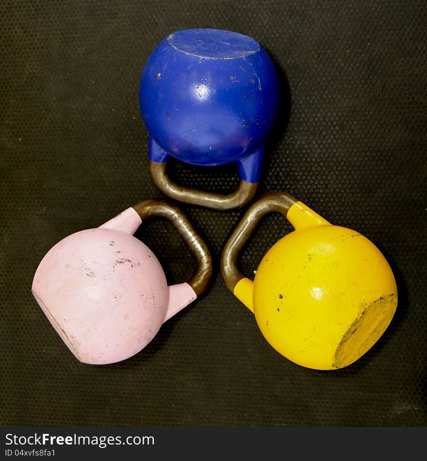 Close up photo of 3 Kettlebells on a gym floor.