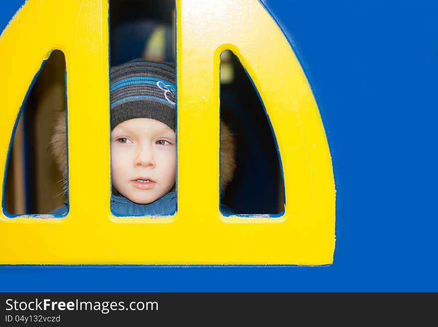 A kid looking from a yellow window on blue wall. A kid looking from a yellow window on blue wall.