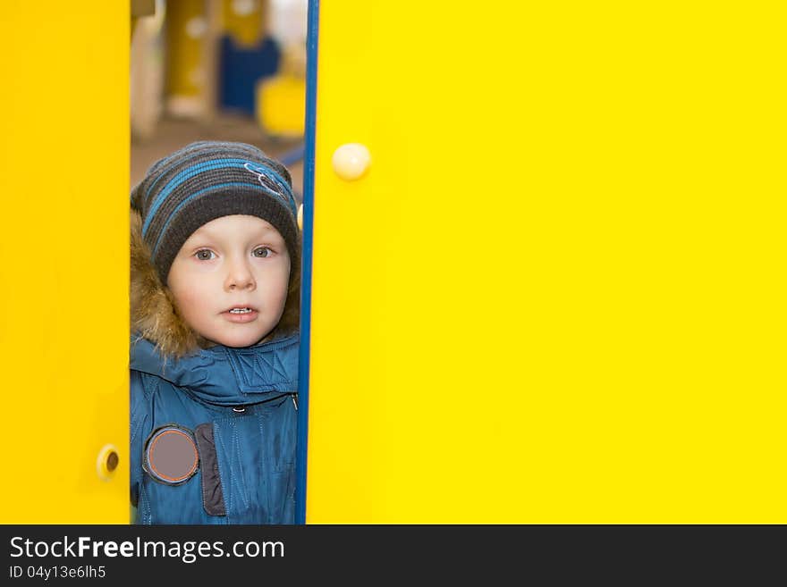 Kid peeping through a gap in two yellow walls at some kid's park.