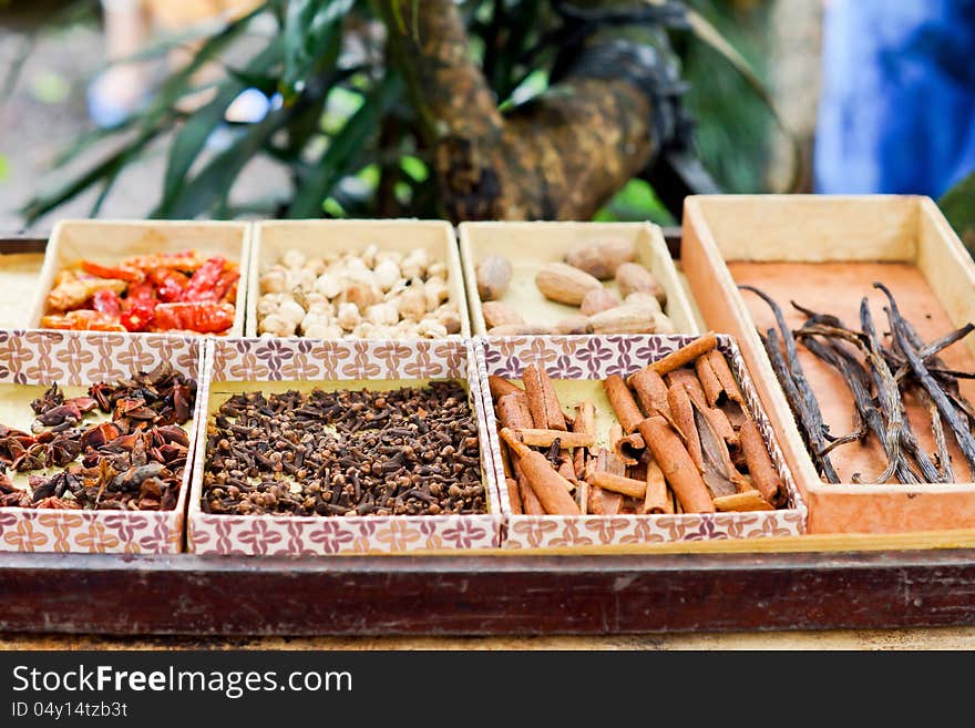 Trays of dried spaces and herbs for sale on a market stall including bark cinnamon, chillies and vanilla pods