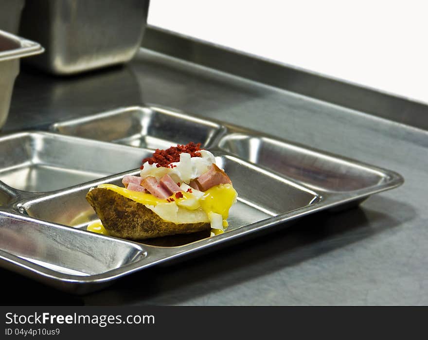 Baked potato with toppings on metal tray in cafeteria. Baked potato with toppings on metal tray in cafeteria