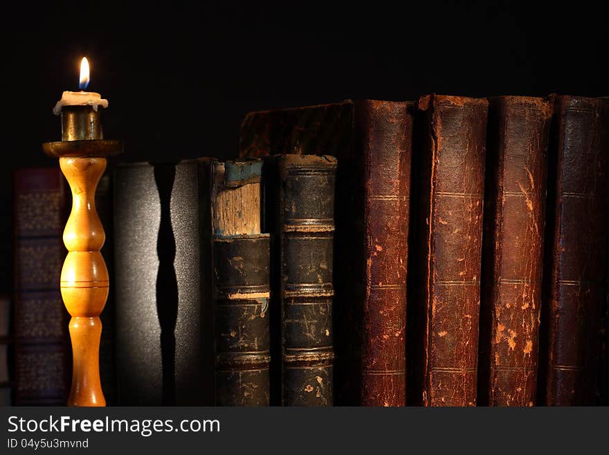 Ancient books in a row near lighting candle on dark background. Ancient books in a row near lighting candle on dark background