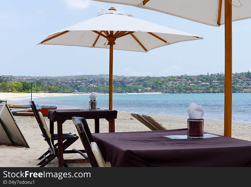 Empty wooden tables and umbrellas on a tropical bay with a long sandy beach for that idyllic vacation. Empty wooden tables and umbrellas on a tropical bay with a long sandy beach for that idyllic vacation