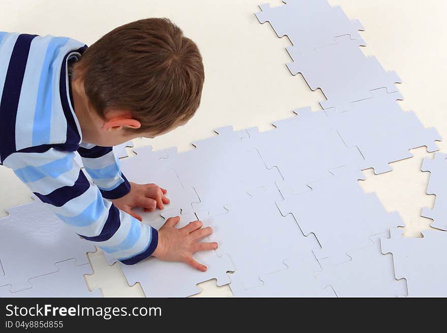 Boy laying an white elements of a jigsaw puzzle on the white background. Boy laying an white elements of a jigsaw puzzle on the white background