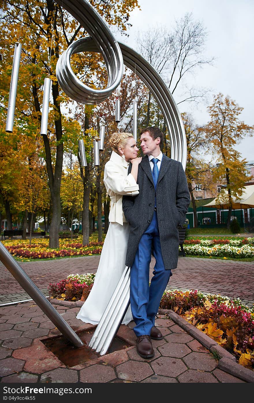 Bride and groom about iron figure on autumn wedding walk