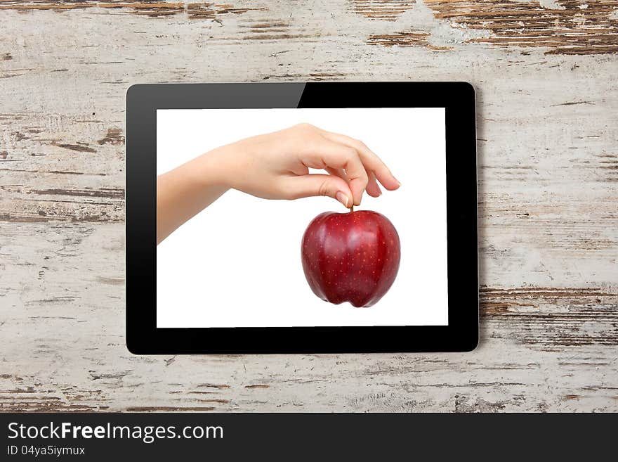 Tablet computer with the hand and a red apple on the screen on a background of wood. Tablet computer with the hand and a red apple on the screen on a background of wood