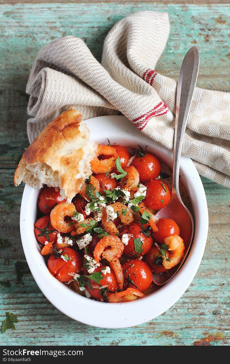 Baked shrimps and cherry tomatoes with feta cheese and fresh parsley in a baking dish with bread