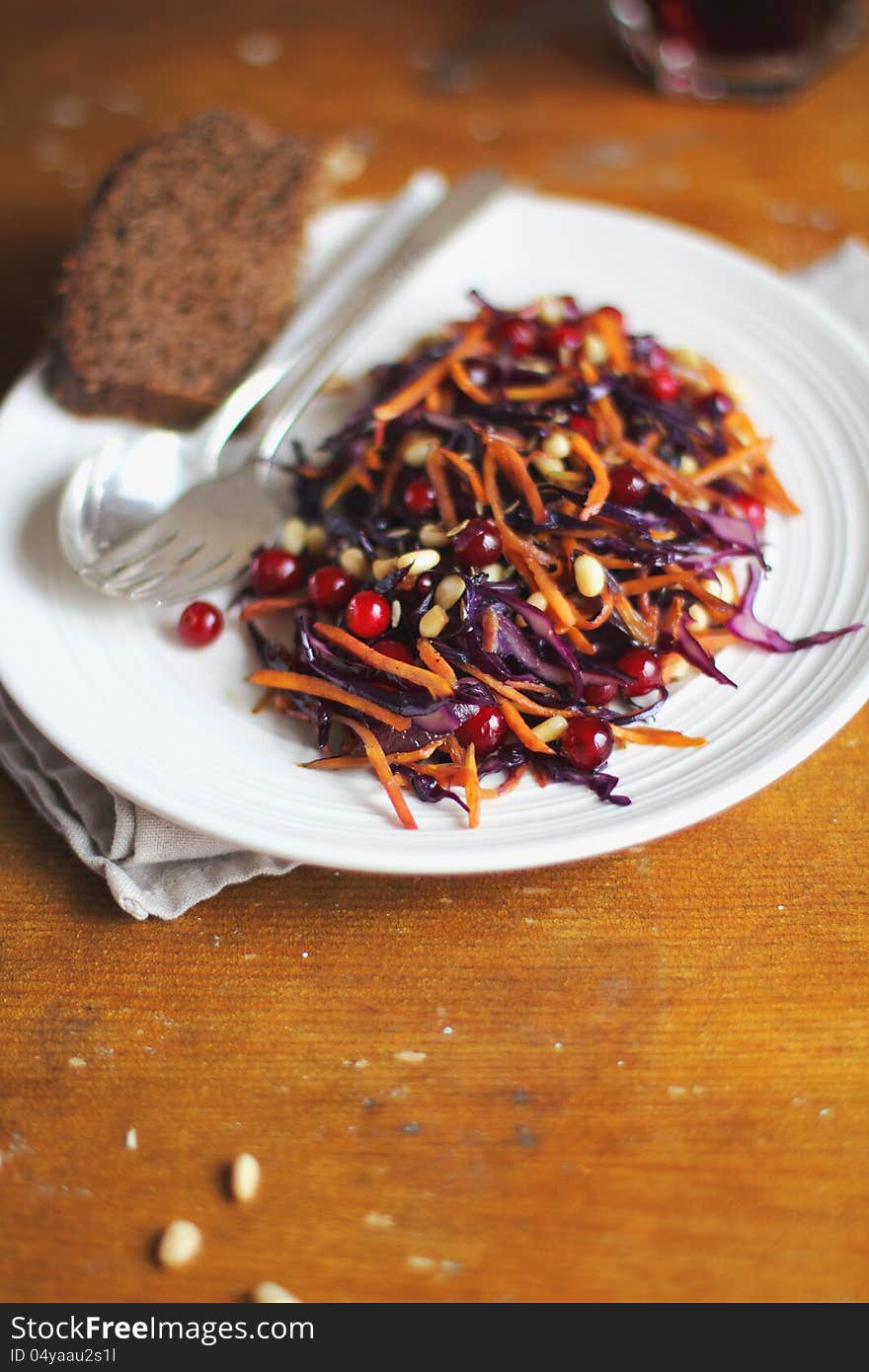 Salad with red cabbage, carrots, cranberry, pine nuts and bread slice on plate. Salad with red cabbage, carrots, cranberry, pine nuts and bread slice on plate