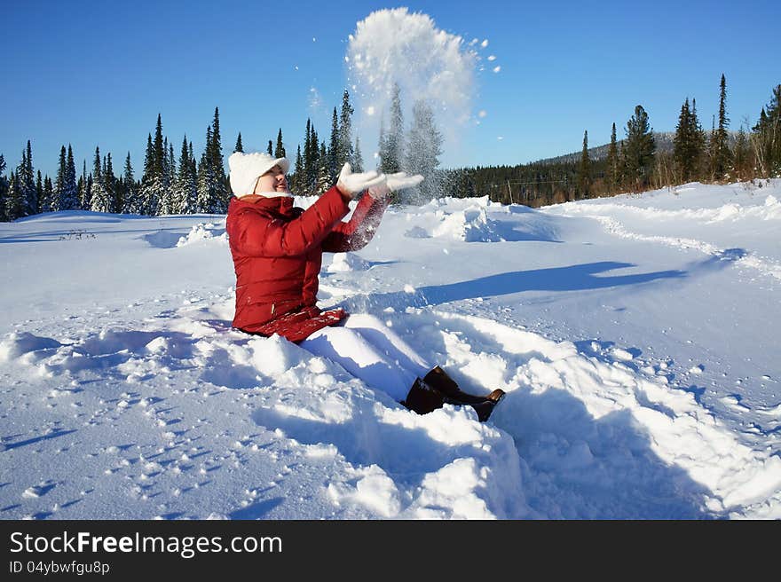 Girl clothed in red jacket, sits in the snow and plays with snow on a sunny winter day. Girl clothed in red jacket, sits in the snow and plays with snow on a sunny winter day.