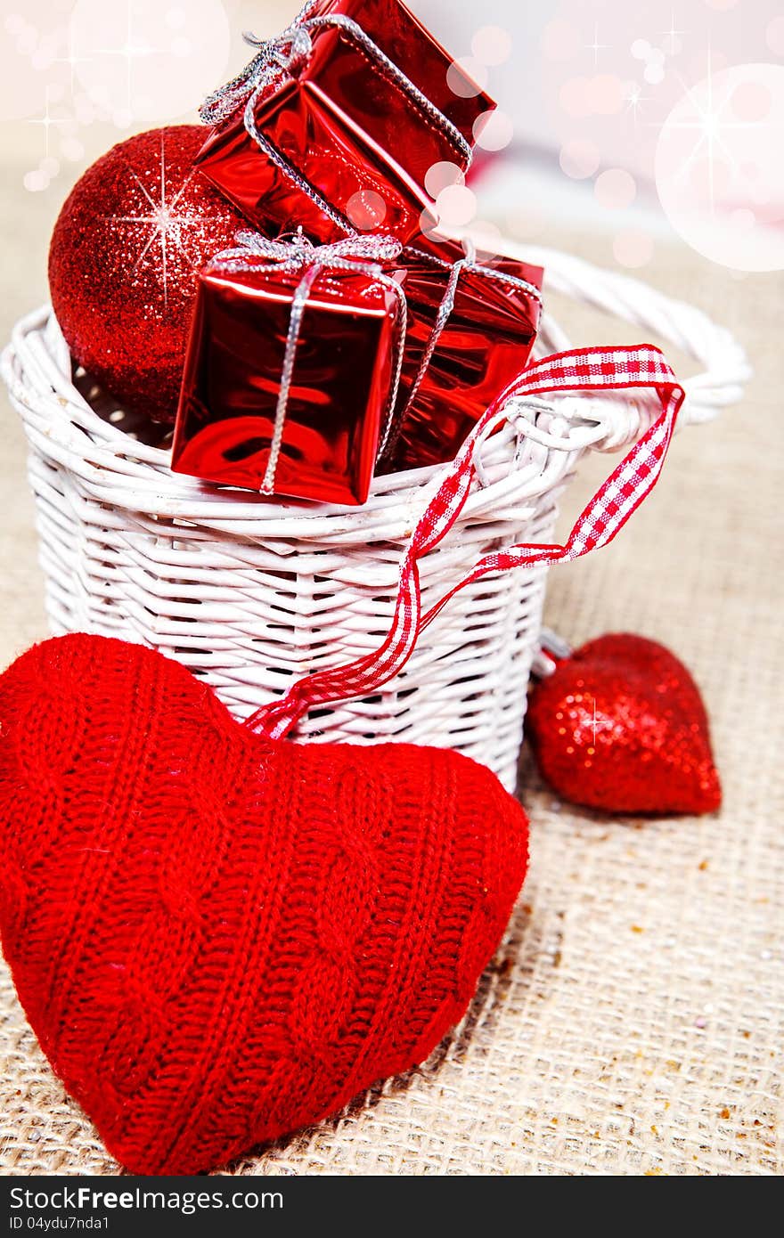 Woolen heart and tiny red presents in a white wicker basket