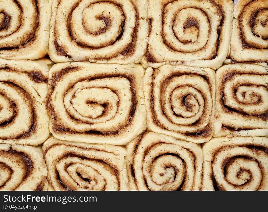 Twelve cinnamon buns in a rectangular tray showing a pattern of spiral swirls and straight edges