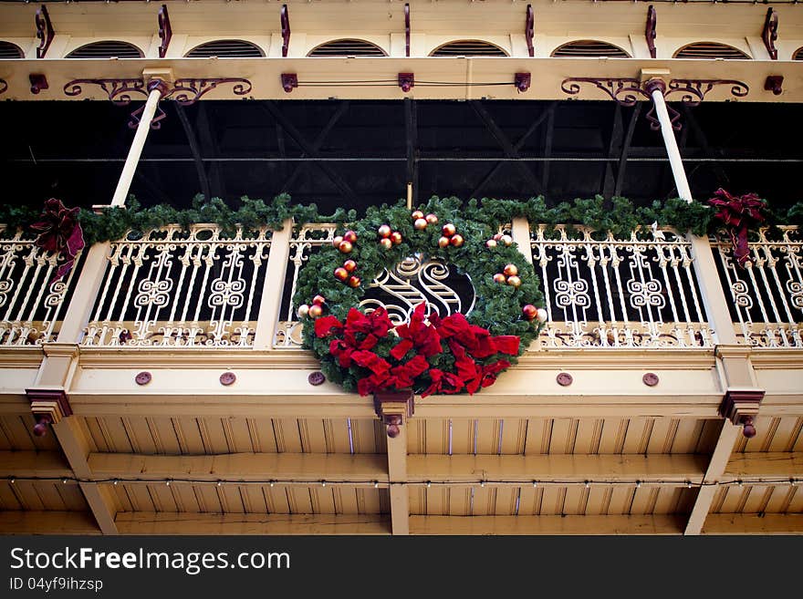 Christmas wreath hung on a late 1800s wrought iron & wood walkway. The wreath is made of green foliage with a red bow & gold decorations throughout. Evergreen garland lines the walkway handrail. Christmas wreath hung on a late 1800s wrought iron & wood walkway. The wreath is made of green foliage with a red bow & gold decorations throughout. Evergreen garland lines the walkway handrail.