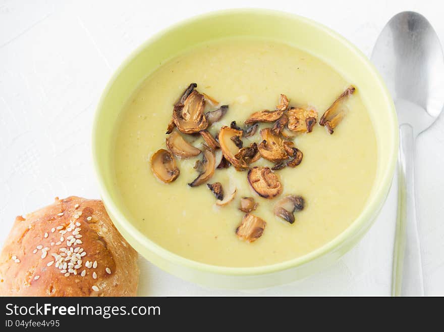 Leek mashed soup with fried sliced mushrooms in the green bowl with bun and spoon. White background.