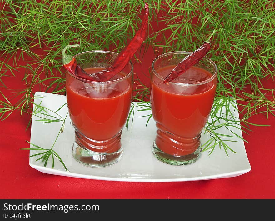 Two glasses of tomato juice with leaves on a white background