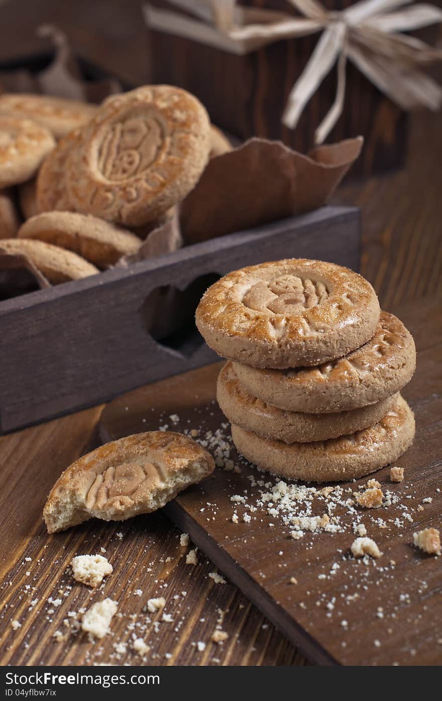 Closeup of cookies in the box and dry roses on wooden board. Biscuits stack and one broken cookie with crumbs on cutting board. Closeup of cookies in the box and dry roses on wooden board. Biscuits stack and one broken cookie with crumbs on cutting board.