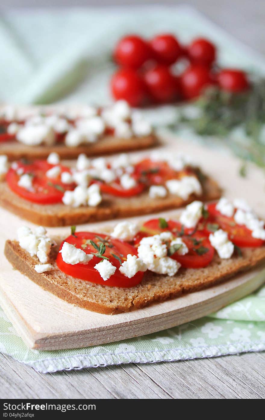 Cherry Tomato and Feta bread slices with Thyme on a wooden cutting board. Cherry Tomato and Feta bread slices with Thyme on a wooden cutting board