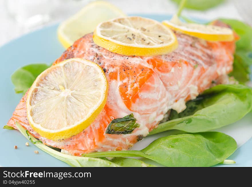 Baked salmon fillet with lemon and spinach on a plate closeup. Baked salmon fillet with lemon and spinach on a plate closeup