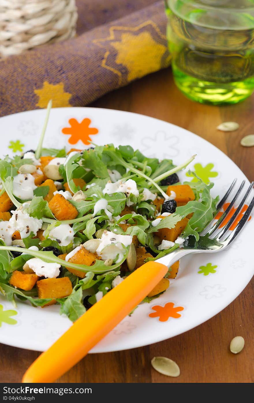 Salad with pumpkin, feta and arugula on a plate closeup vertical