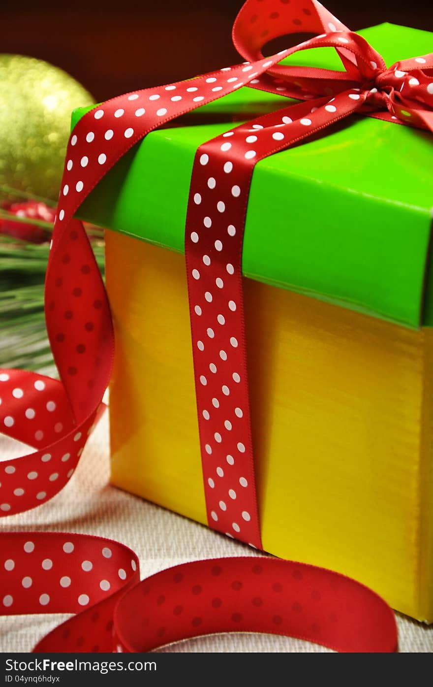 Yellow and green Christmas holiday present gift wrapped with red polka dot ribbon and holly decoration on white and grey striped tablecloth (Close-up). Yellow and green Christmas holiday present gift wrapped with red polka dot ribbon and holly decoration on white and grey striped tablecloth (Close-up)