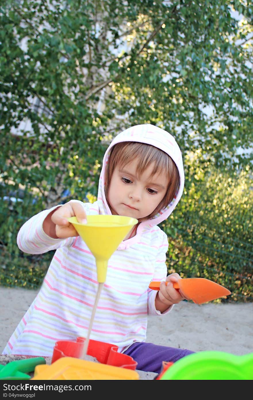 Little pretty girl while playing with funnel and sand, studying physics