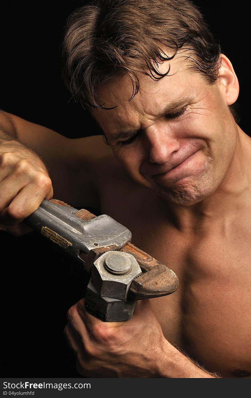 Muscular shirtless man struggles to loosen a big nut with a pipe wrench. Muscular shirtless man struggles to loosen a big nut with a pipe wrench