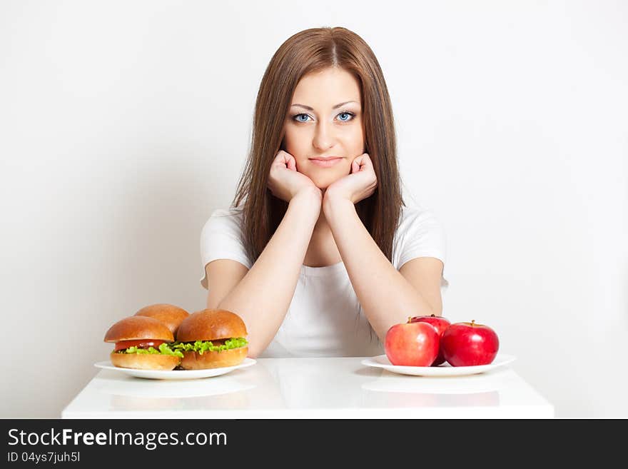 Woman sitting behind the table with standing junk food and apples. Woman sitting behind the table with standing junk food and apples