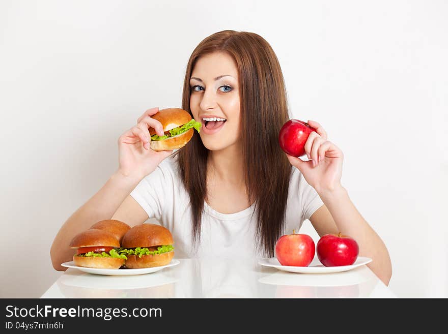 Woman try to eat a hamburger and holding apple to. Woman try to eat a hamburger and holding apple to