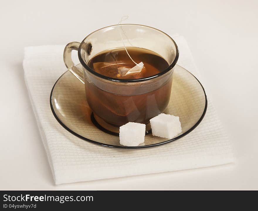 Cup of tea and two slices of sugar on a saucer on a white napkin. Cup of tea and two slices of sugar on a saucer on a white napkin