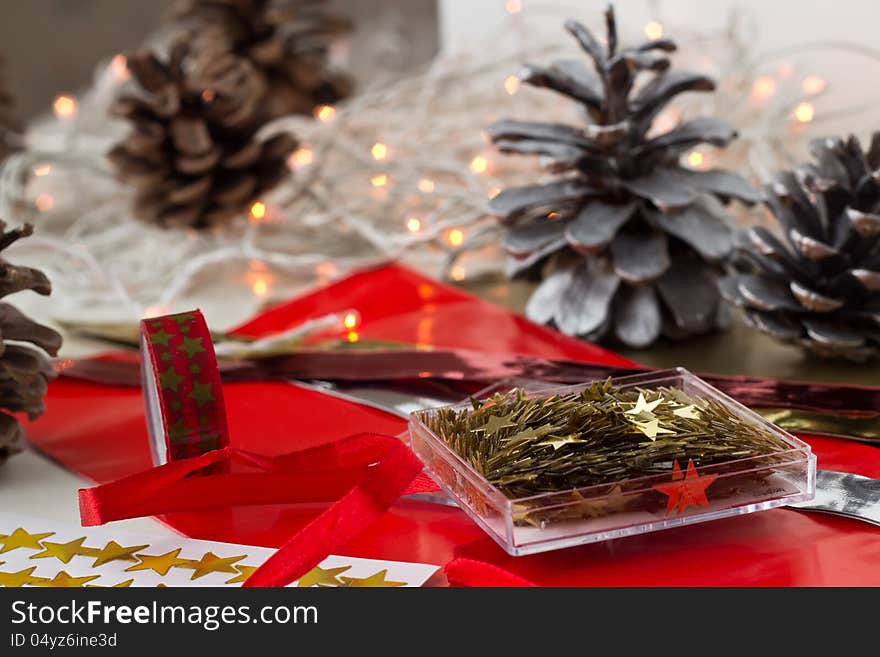 Christmas decoration stars, paper, masking tape prepared on the table. Christmas light and silver cones are on the background. Christmas decoration stars, paper, masking tape prepared on the table. Christmas light and silver cones are on the background.