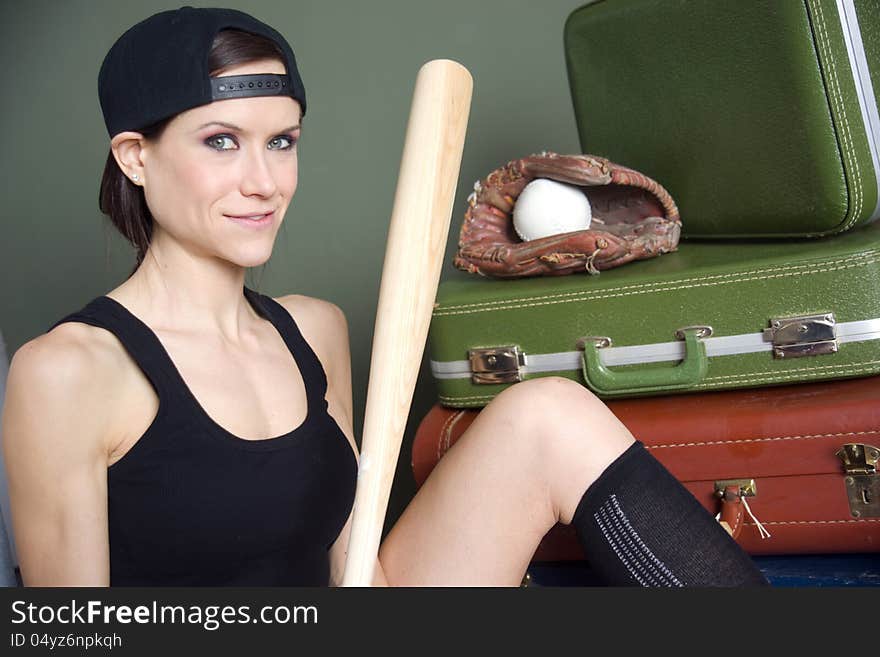 An attractive woman sits in front of her luggage with her baseball gear. An attractive woman sits in front of her luggage with her baseball gear