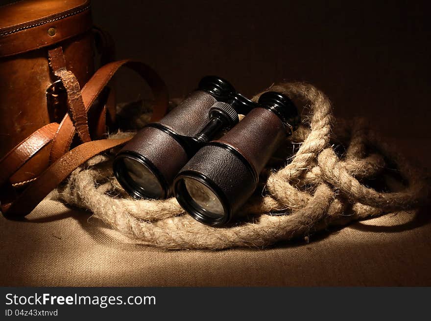 Still life with old binoculars on hemp rope near leather case