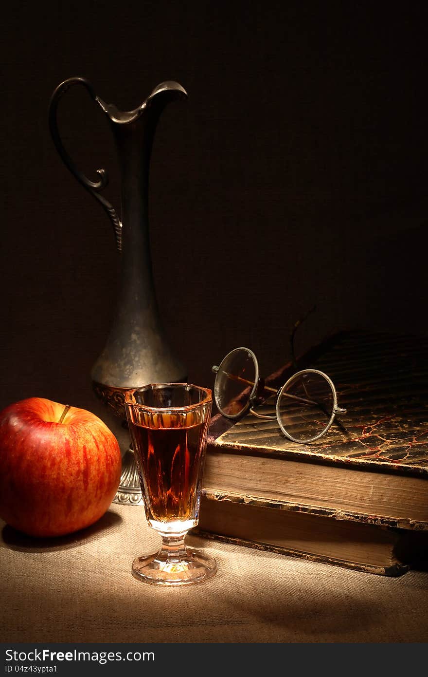 Vintage still life with apple and drink near old book on canvas surface