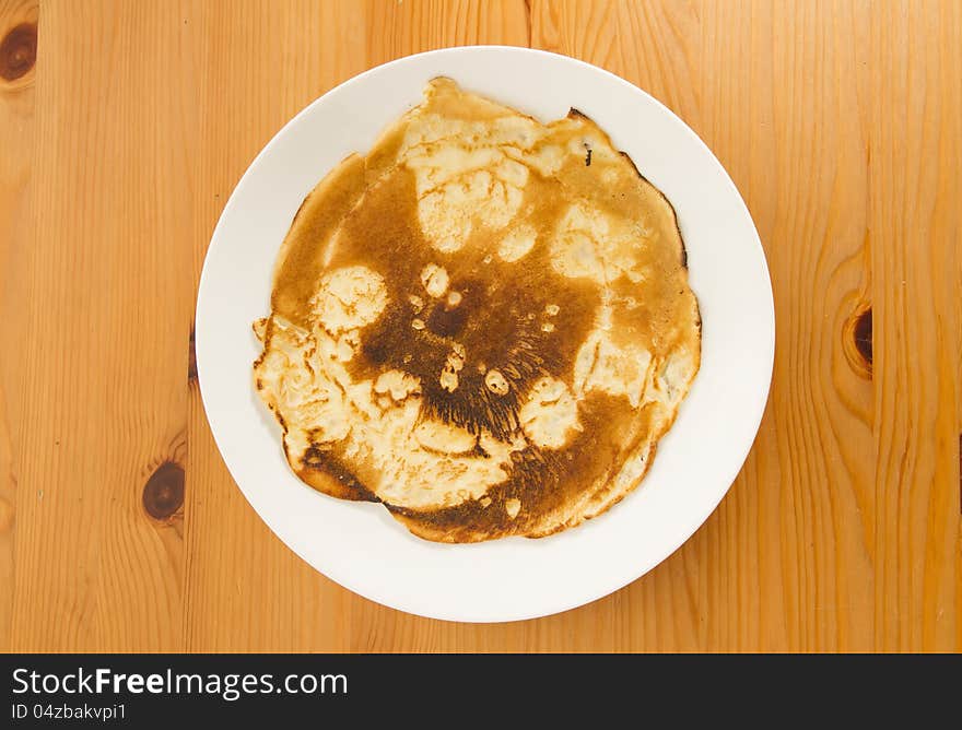 Top view on burnt pancake on white plate