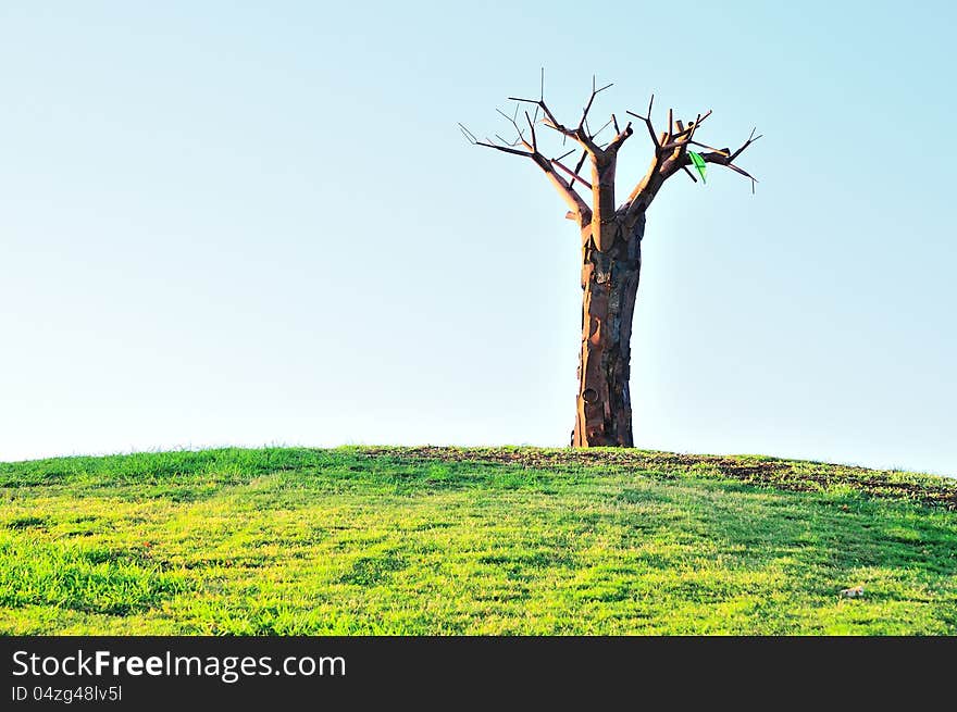 On top of a hill covered with green grass is a sculpture made of wood and metal. On top of a hill covered with green grass is a sculpture made of wood and metal