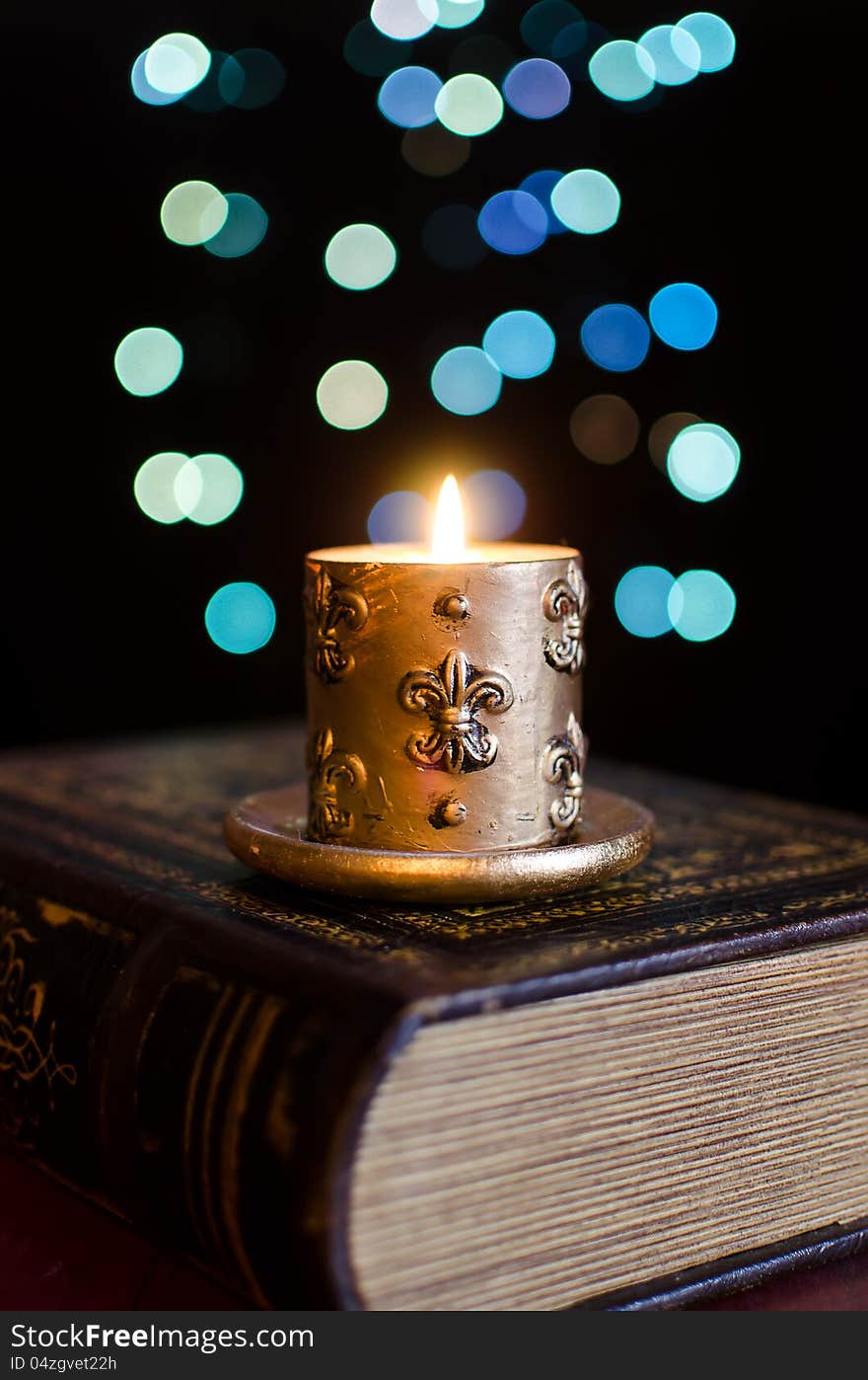 Burning candle and old book on bokeh background