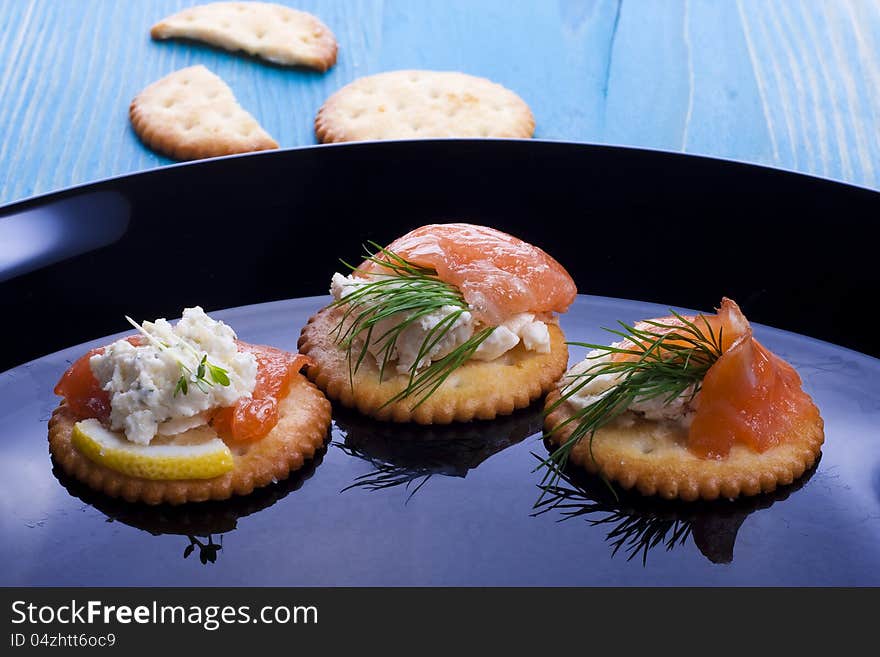 Light snack from smoked salmon with soft cheese and herbs on crackers.