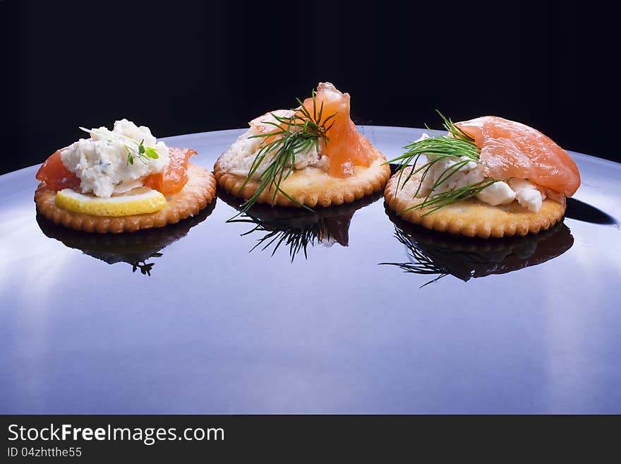Light snack from smoked salmon with soft cheese and herbs on crackers.